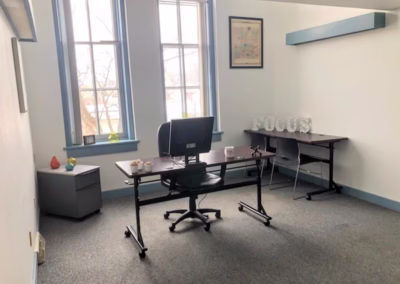 A photo of a large private office with a desk, chair, monitor, and large windows.